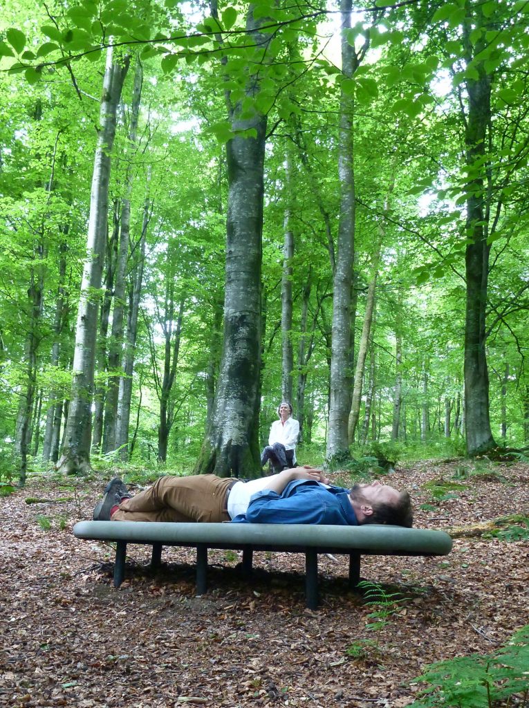 Two people interacting with Rosnes Benches in broadleaf woodland at Gatehouse of Fleet,