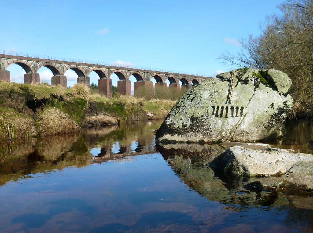 Cairnsmore of Fleet National Nature Reserve including the Big Water of Fleet Viaduct and a piece of environmental art in the foreground - arches sculpted into a river boulder.
