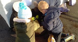 A group of children planting bulbs in a large half-barrel planter.